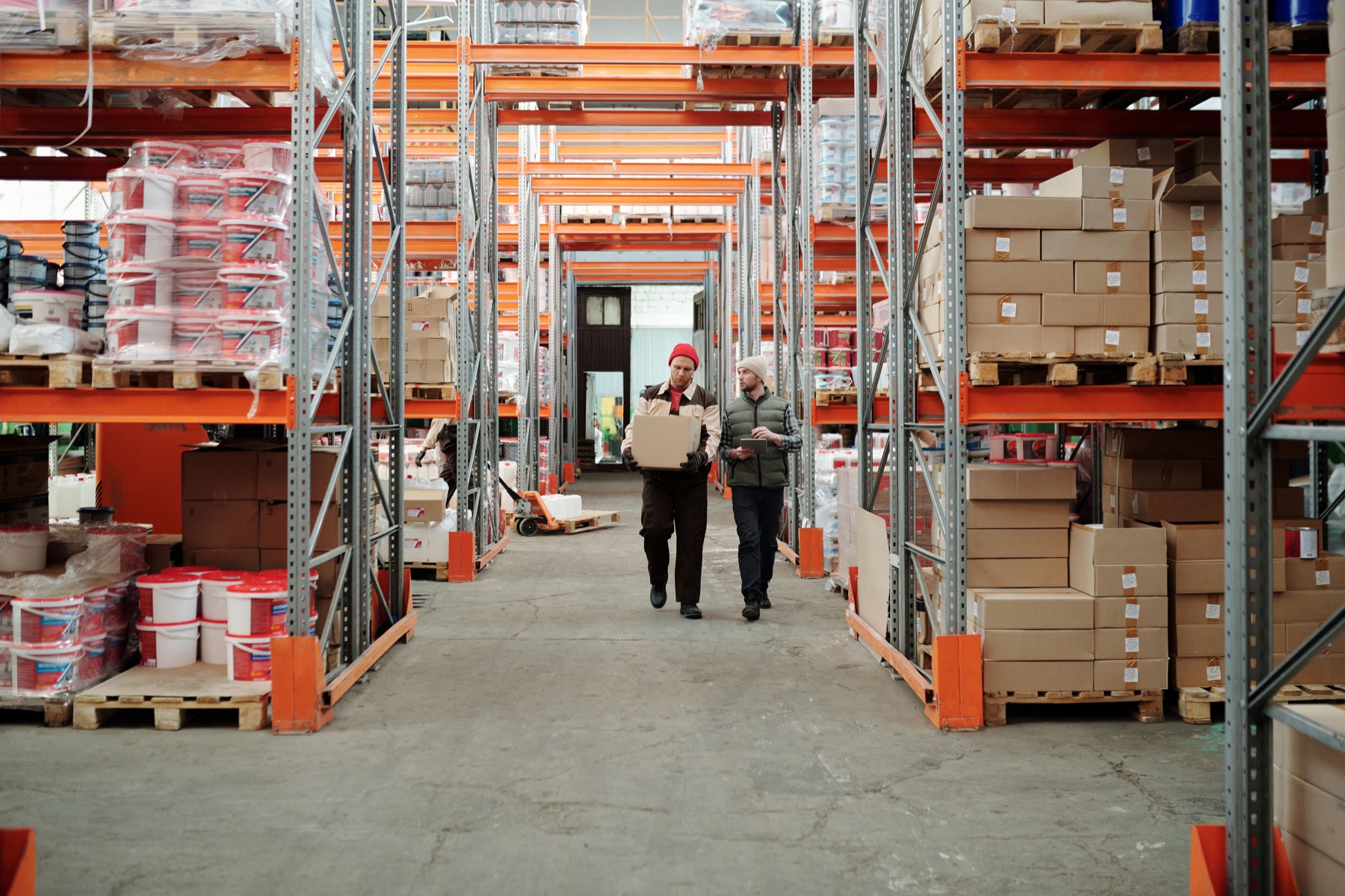 Two workers handling a package in a warehouse aisle.
